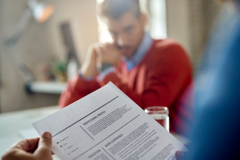 A man reviews a resume while another man sits at a table, highlighting tips for crafting a stand out CV.