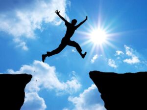 discovering your passion. Silhouette of a person leaping between two cliffs against a bright blue sky with sun rays. Conveys courage, determination, and freedom.