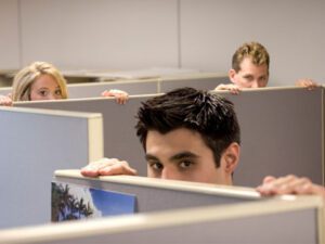 HR Manager Three individuals peer over office cubicle walls, appearing curious and amused. The scene conveys a playful tone in a typical office environment.