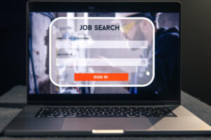 A person using a laptop to search for job opportunities online, with a focused expression and a notepad beside them.